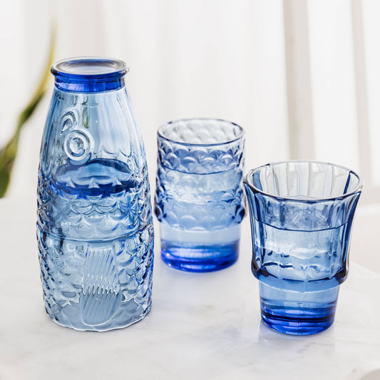 Set of blue glass bottles and tumblers on a light surface with a blurred background