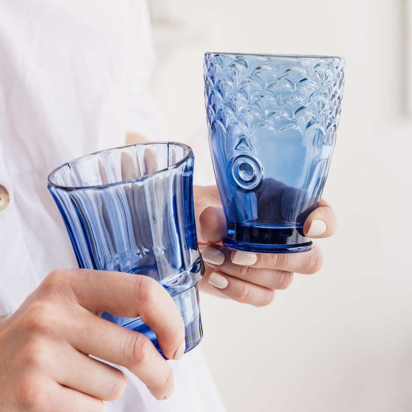 Two hands holding blue glass tumblers with a white background
