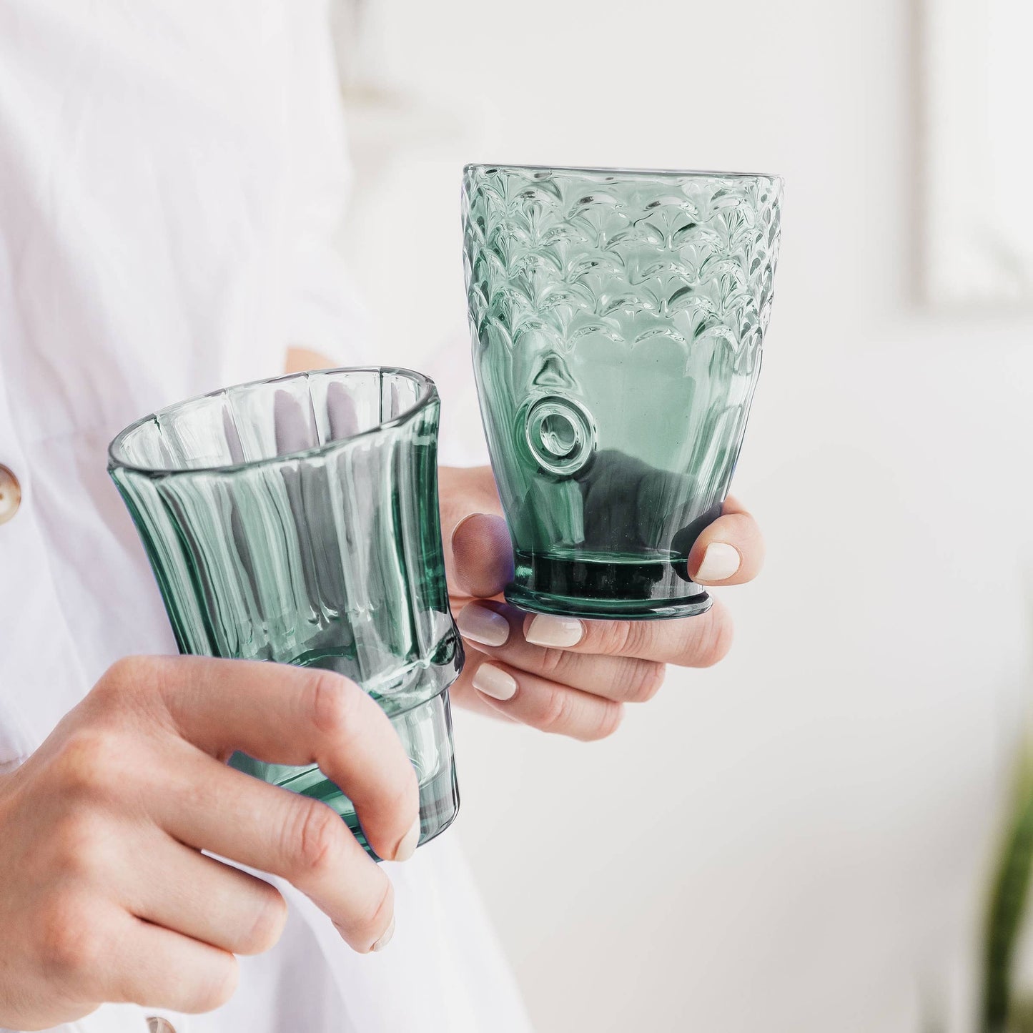 Two hands holding green glass tumblers against a light background