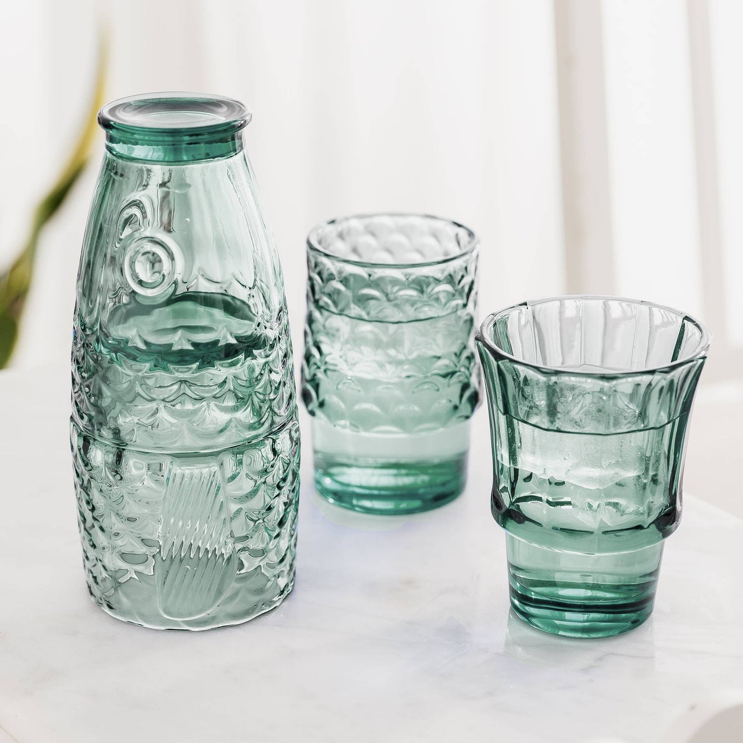 Set of green glass bottles and tumblers on a light background