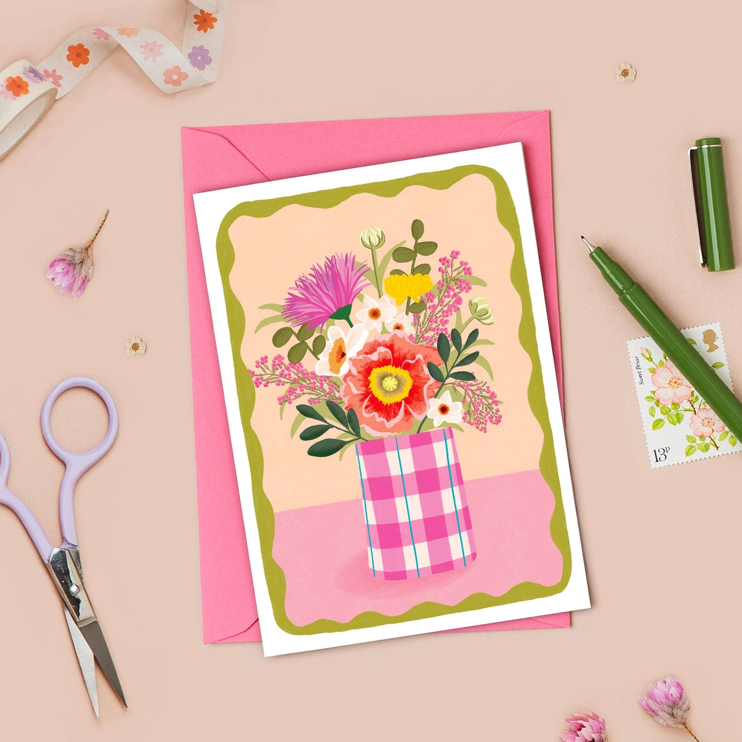 Floral card with pink envelope on a beige background with stationery items.