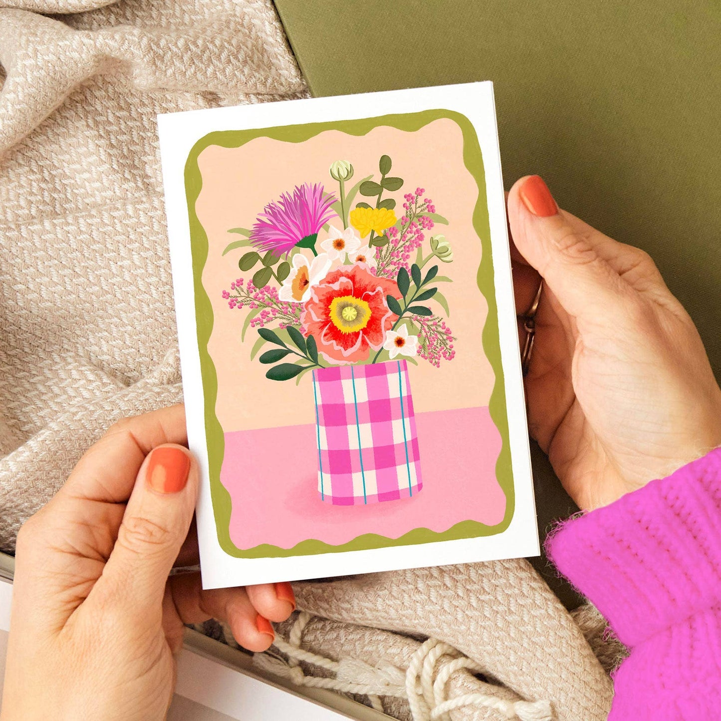 Hand holding a card with floral design and plaid pattern on a textured surface