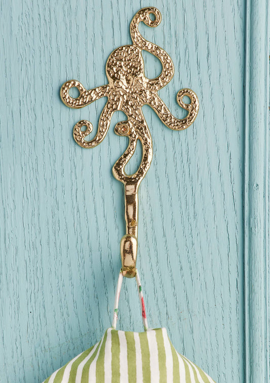 A gold octopus-shaped hook hanging on a light blue painted wooden door, with a green and white striped fabric item suspended from it.