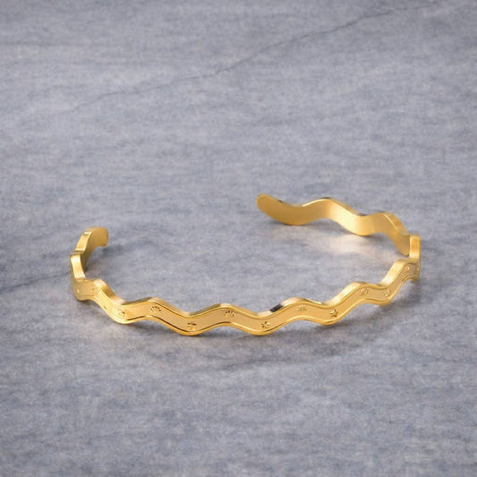 Gold bracelet with wavy design on a gray background