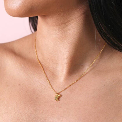 Gold necklace with a small pendant worn by a person against a pink background