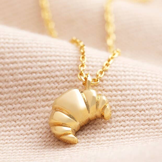 Gold croissant-shaped pendant necklace on a beige fabric background