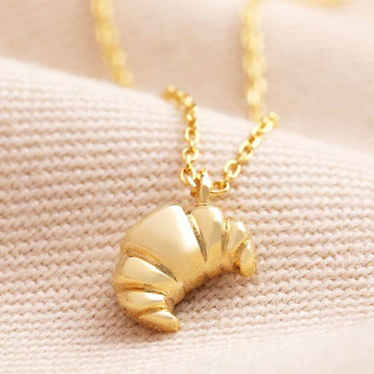 Gold croissant-shaped pendant necklace on a beige fabric background