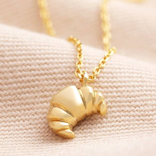 Gold croissant-shaped pendant necklace on a beige fabric background
