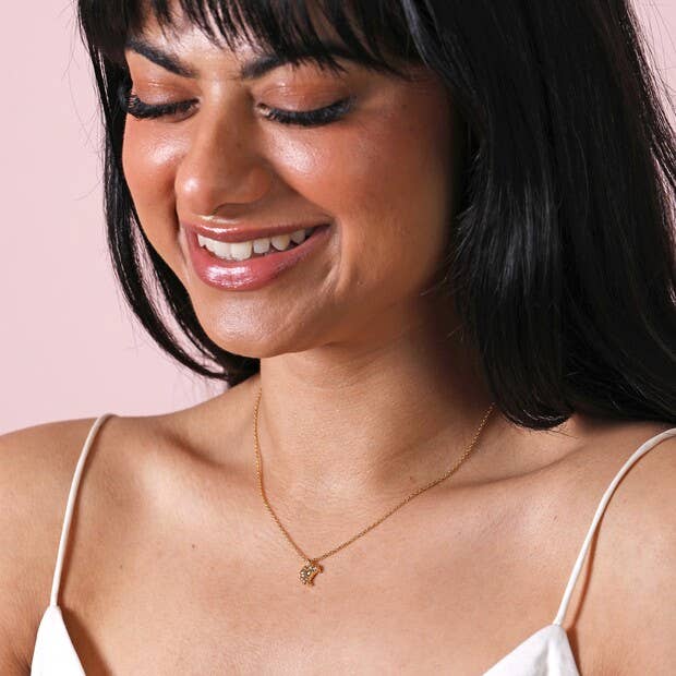 Woman wearing a gold necklace with a pink background