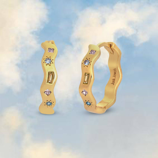Gold hoop earrings with gemstones against a cloudy sky background