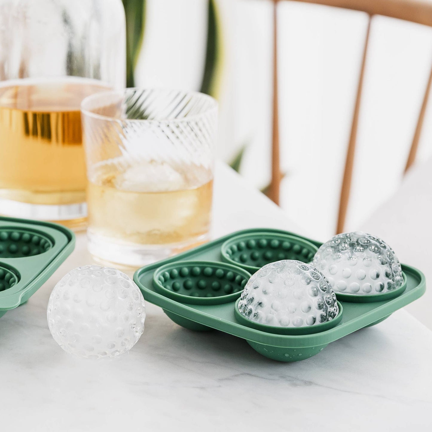 Green silicone ice ball mold with formed ice balls on a table with drinks in the background