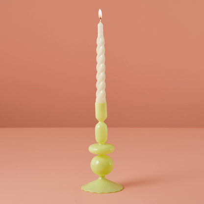 Tall candle with a textured white wick on a green candlestick against a pink background
