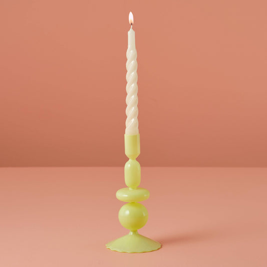 Tall candle with a textured white wick on a green candlestick against a pink background