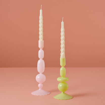 Two decorative candles with unique designs on a pink background