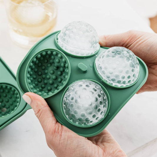 Green silicone ice ball mould with clear silicone balls inside, held by a hand.