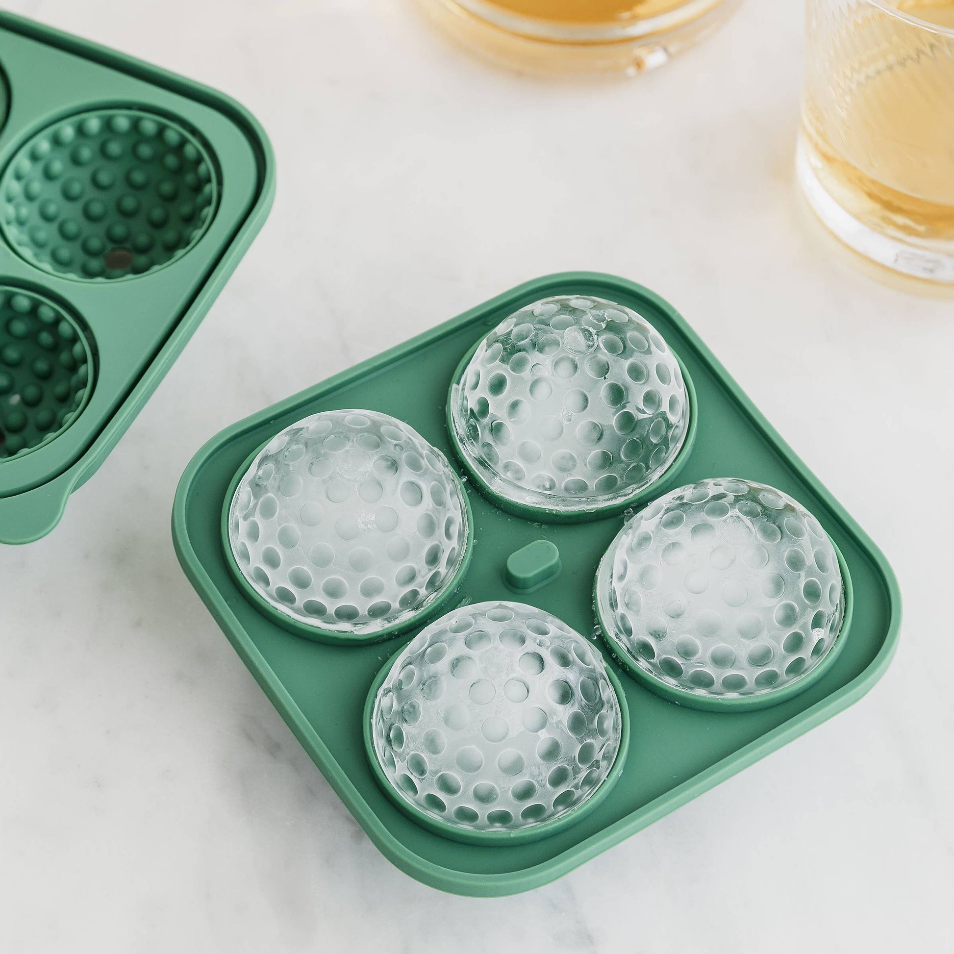 Green silicone ice mold tray with spherical molds on a light surface.