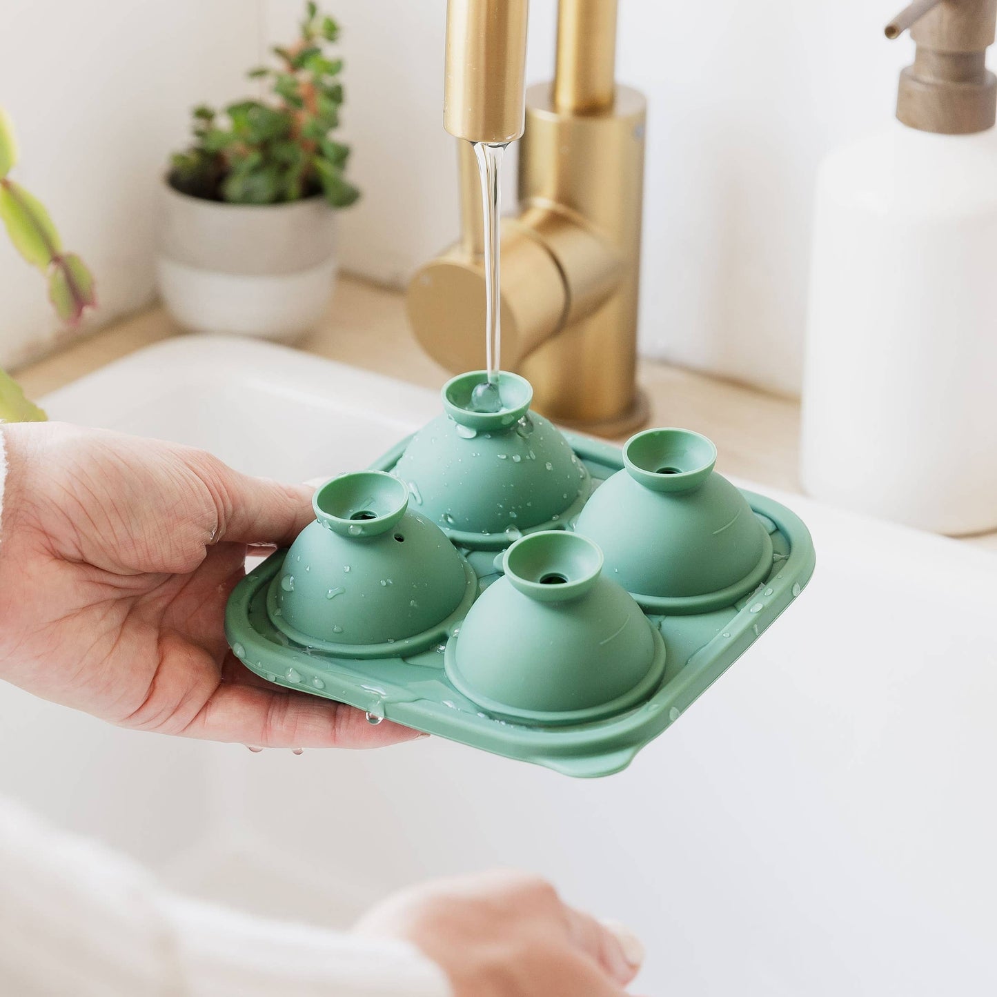Green silicone ice mould being held over a sink with water running from a faucet.