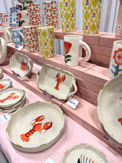 Display of ceramic items with lobster design on a pink shelf