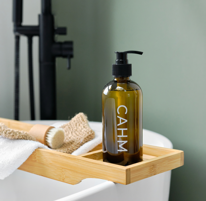 Brown bottle with pump labeled 'CAHM' on a wooden tray over a bathtub.