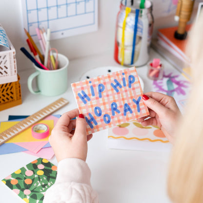 Person holding a colorful card with 'HIP HIP HORAY' text in a classroom setting.