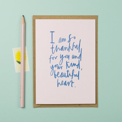 Greeting card with blue text on a light pink background, next to a pink pencil and small yellow card with a daisy on a light green background.