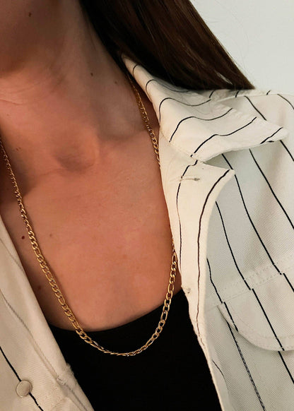 Close-up of a person wearing a gold chain necklace with a blurred background