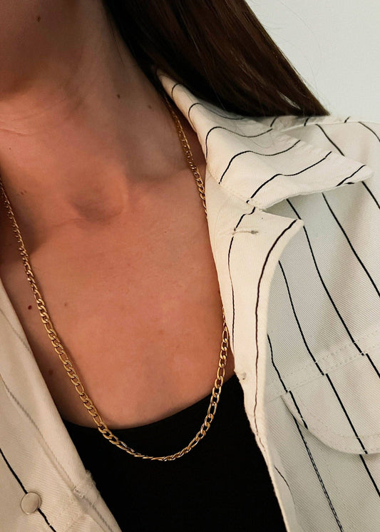 Close-up of a person wearing a gold chain necklace with a blurred background
