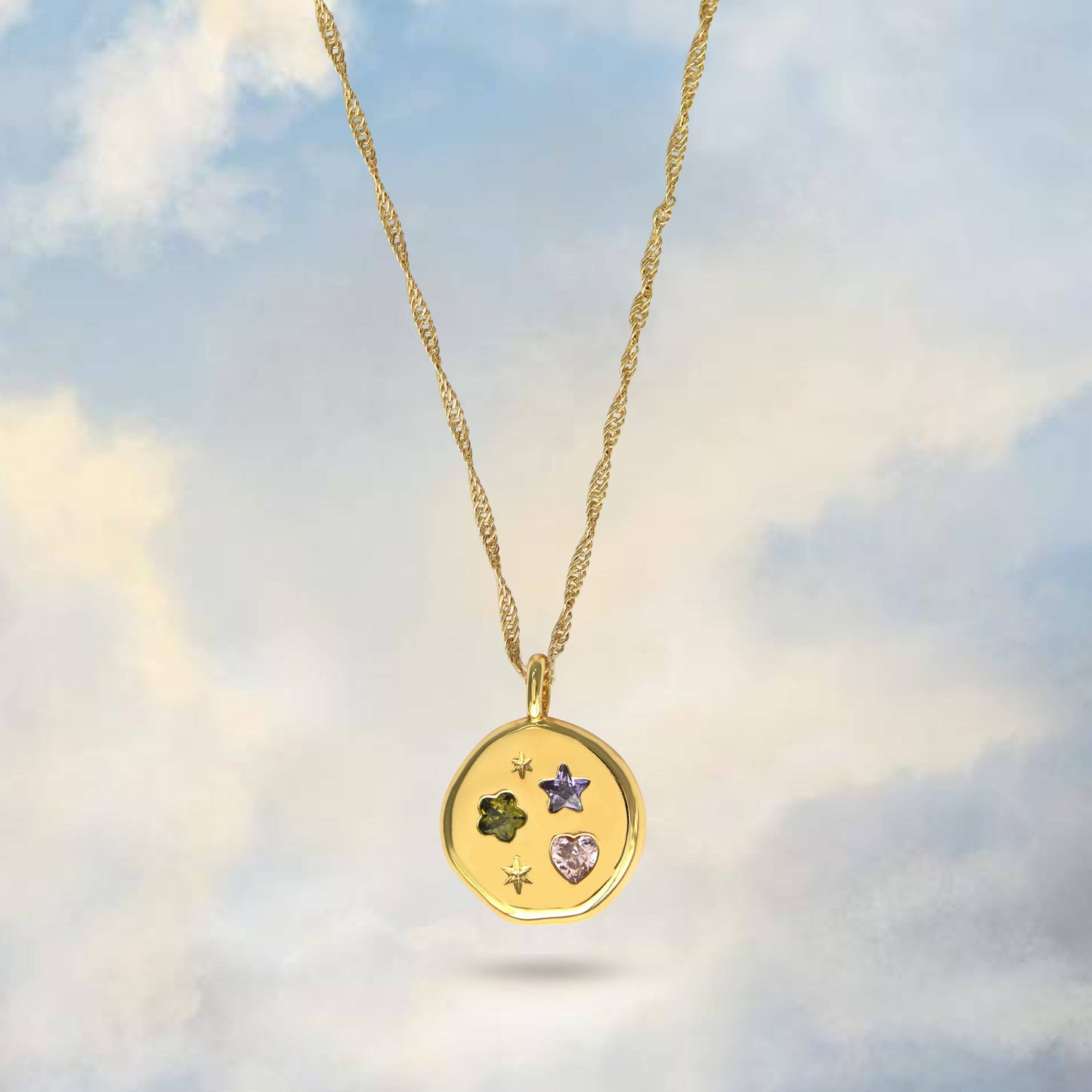 Gold necklace with a pendant featuring embedded stones against a cloudy sky background