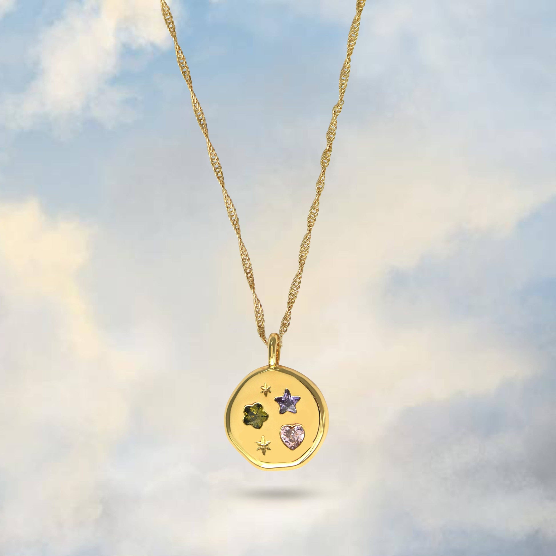Gold necklace with a pendant featuring embedded stones against a cloudy sky background