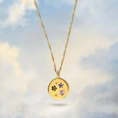 Gold necklace with a pendant featuring embedded stones against a cloudy sky background
