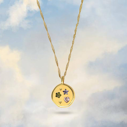 Gold necklace with a pendant featuring embedded stones against a cloudy sky background