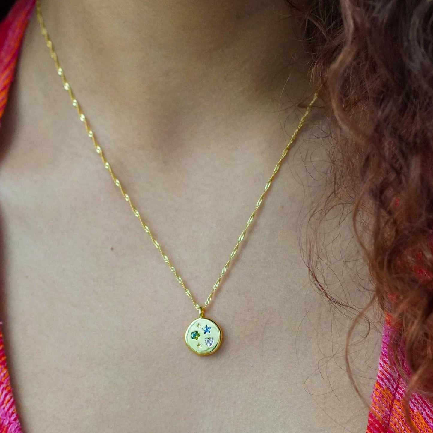Gold necklace with a colorful pendant on a person wearing a multicolored top.