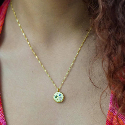 Gold necklace with a colorful pendant on a person wearing a multicolored top.
