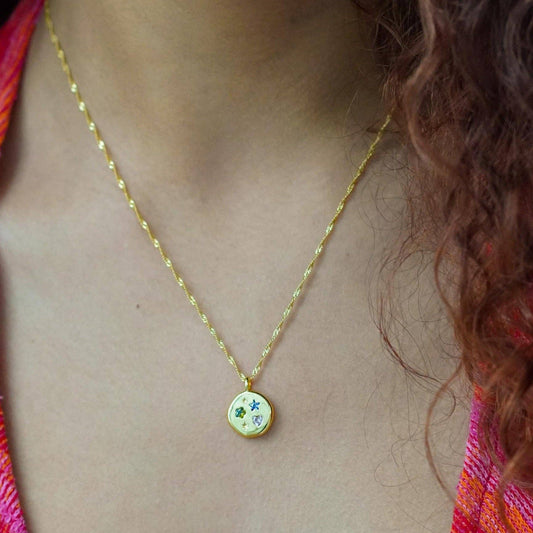 Gold necklace with a colorful pendant on a person wearing a multicolored top.