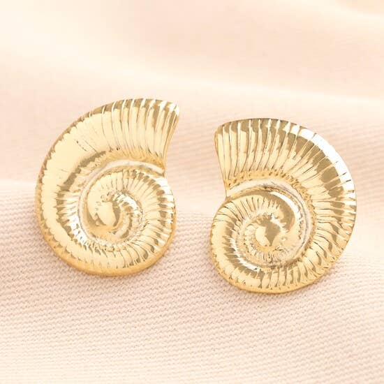 Gold shell-shaped earrings on a light pink fabric background