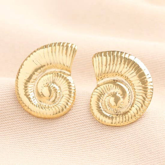 Gold shell-shaped earrings on a light pink fabric background