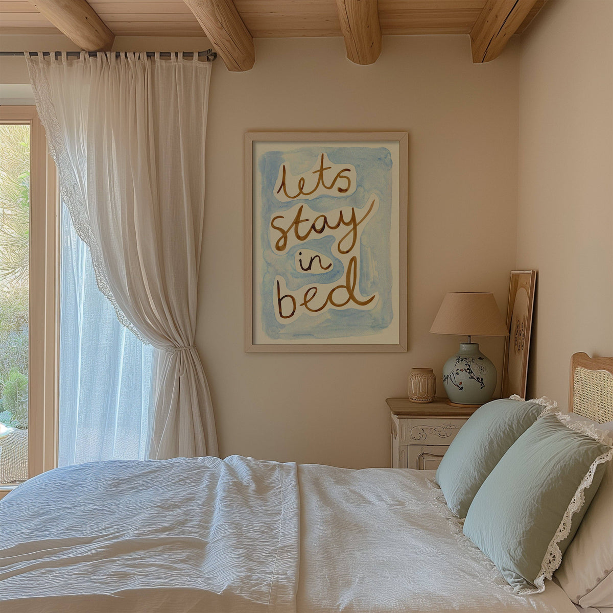 Bedroom with 'Let's stay in bed' artwork on the wall, white bedding, and a lamp.