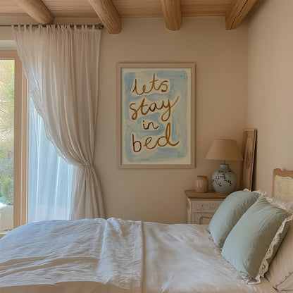 Bedroom with 'Let's stay in bed' artwork on the wall, white bedding, and a lamp.