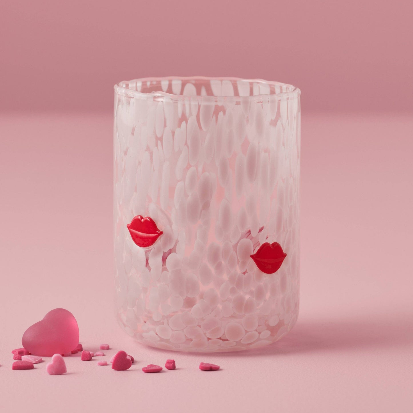 Clear glass with red lip prints on a pink background