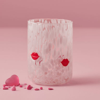 Clear glass with red lip prints on a pink background