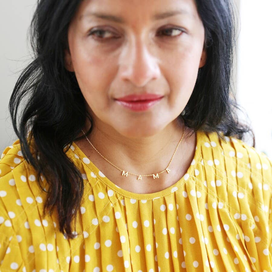 Woman wearing a yellow polka dot top with a necklace that reads 'MAMA'.