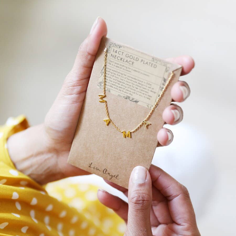 Gold necklace on a brown card held by a person wearing a yellow polka dot shirt.