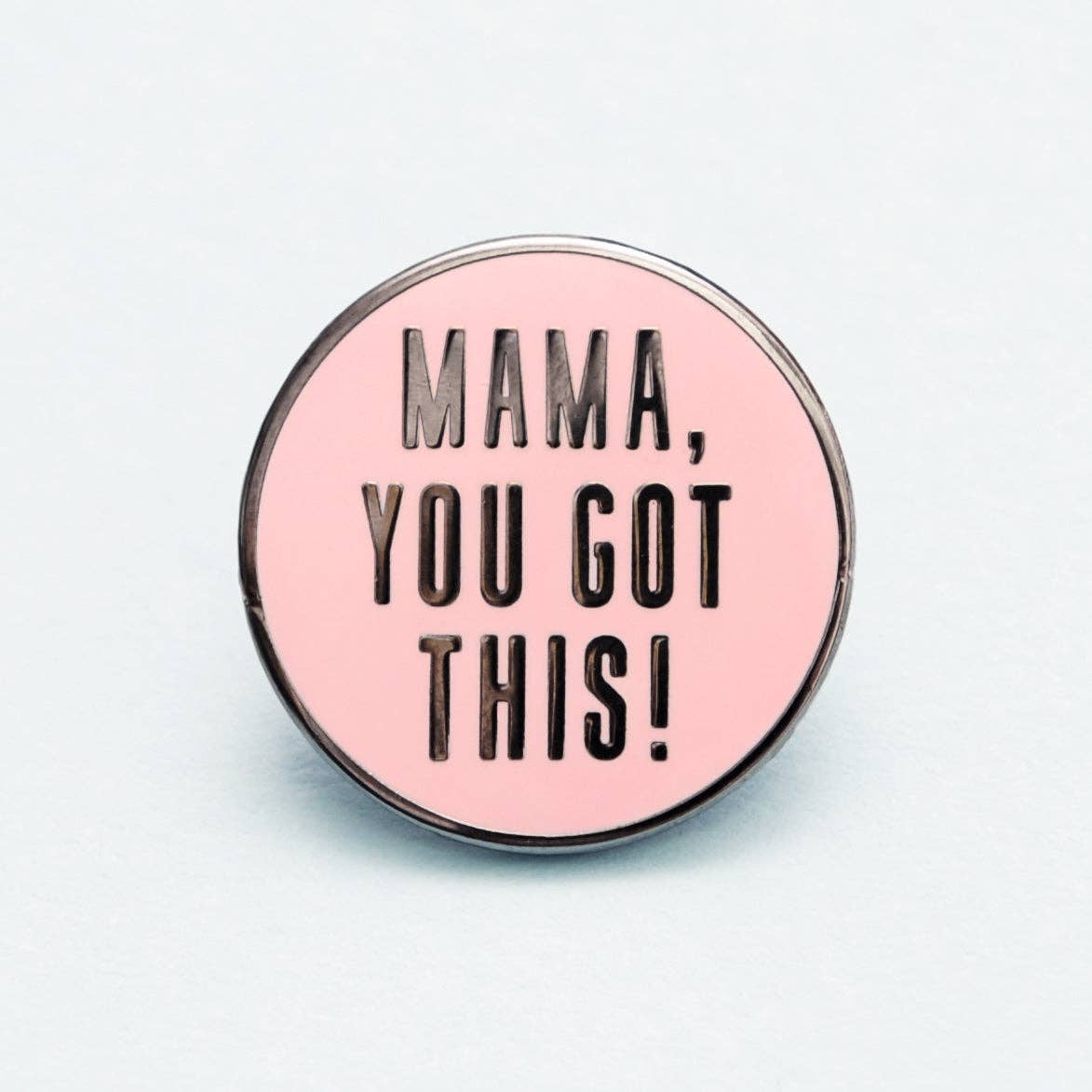Pink enamel pin with 'Mama, you got this!' text on a light gray background