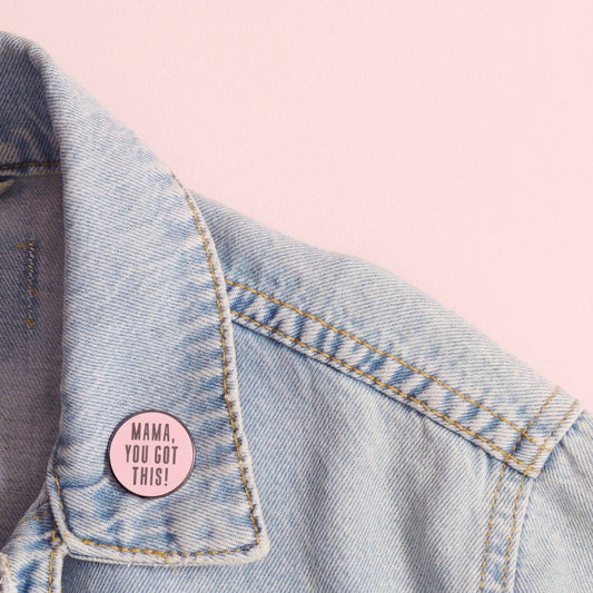 Pink button with 'MAMA, YOU GOT THIS!' text on a denim jacket against a pink background