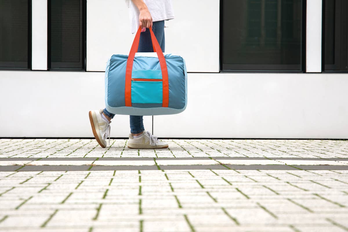 Person holding a blue duffel bag with orange straps on a sidewalk.
