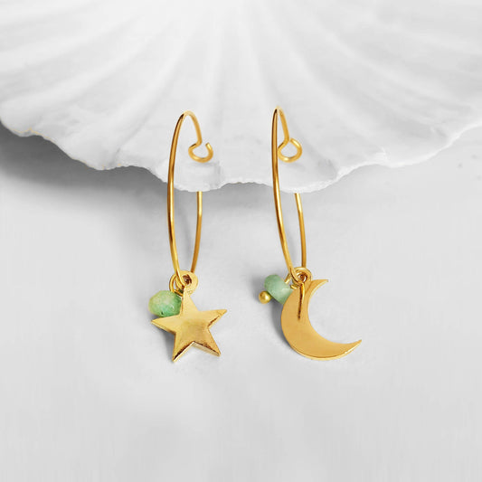 Gold earrings with star and moon charms on a white background