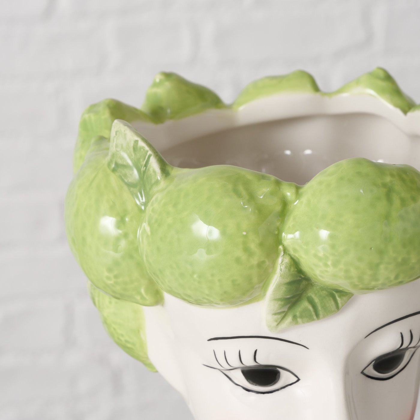 Decorative vase shaped like a face with green lime hair on a white background