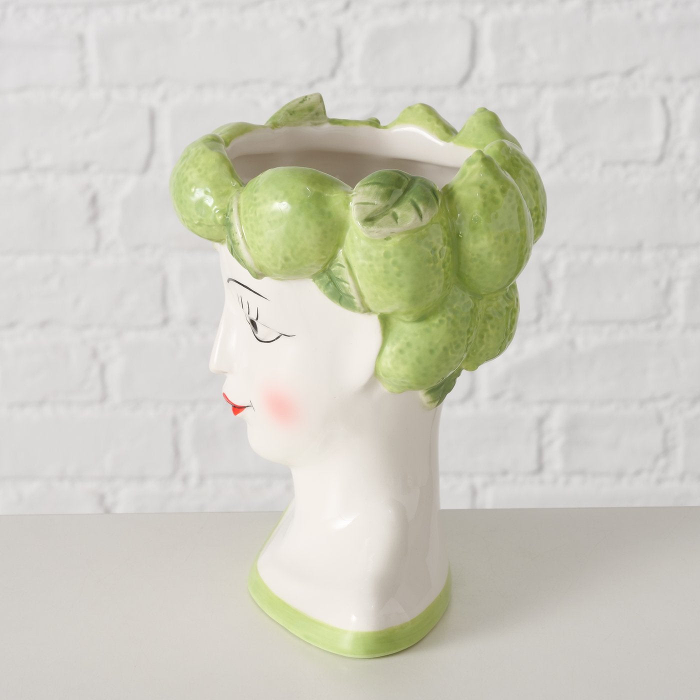 Vase shaped like a woman's head with green lime hair against a white brick wall background