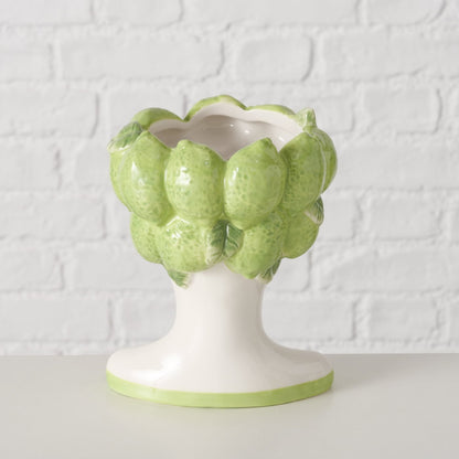 Decorative vase shaped like a cluster of green limes on a white pedestal against a textured white background.