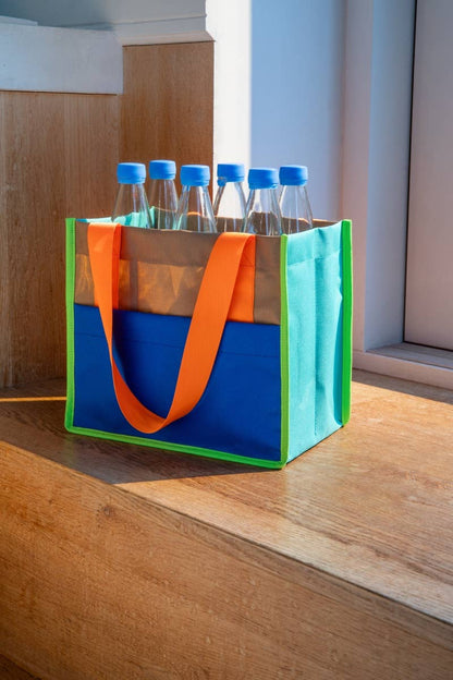 Colorful tote bag with orange handles and blue base containing bottles on a wooden surface.